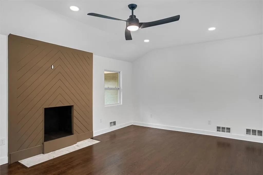 Unfurnished living room with vaulted ceiling, ceiling fan, a large fireplace, and hardwood / wood-style floors