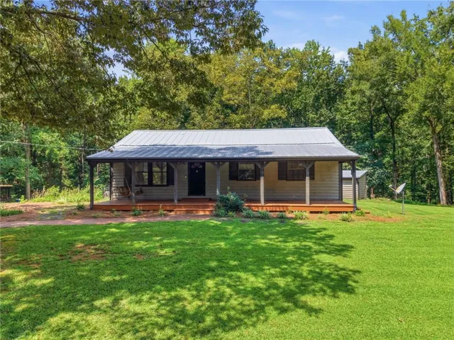 Metal roof, wood-plank siding, covered front porch with wood flooring, dark-framed windows, and a detached shed