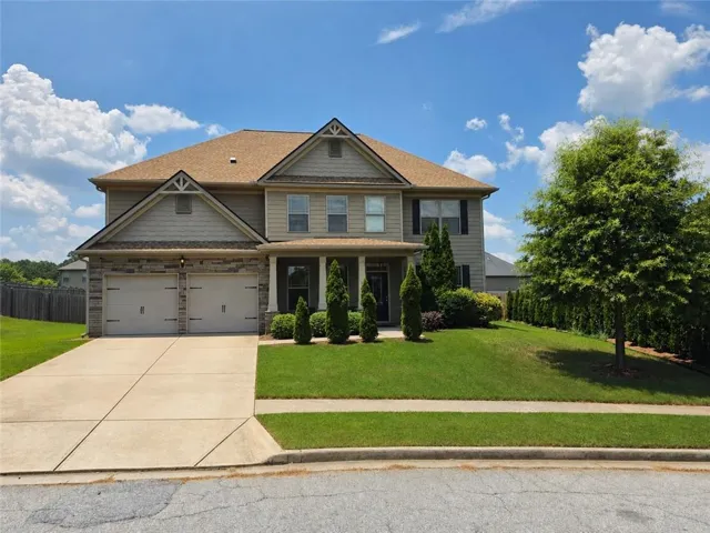 Two-story residence featuring a combination facade of stone veneer and siding, a covered front entry with columns, a two-car garage, a concrete driveway, and a verdant lawn with mature landscaping