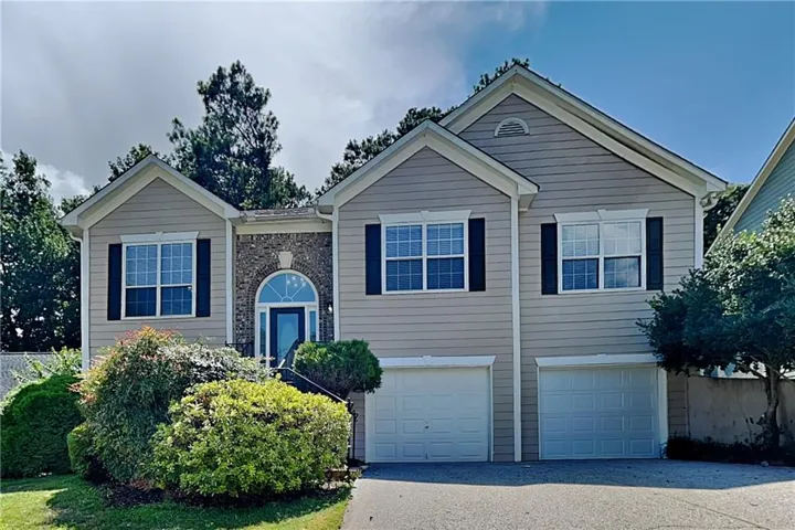 Exterior with light-toned siding, brick accents, arched entry, multiple windows with shutters, and two garage doors