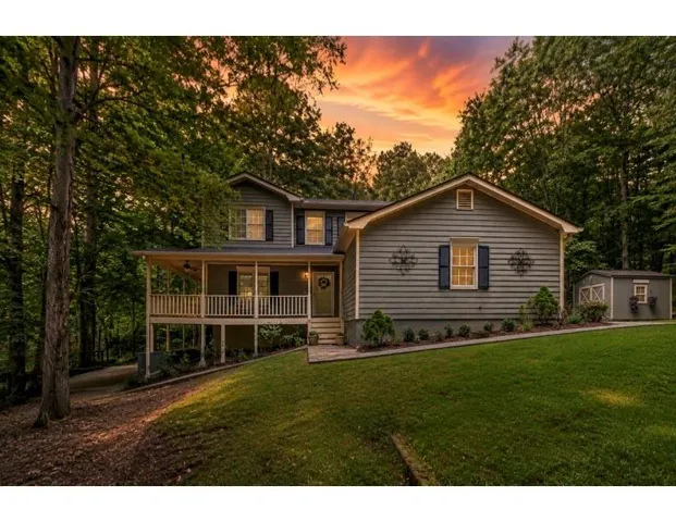 Siding exterior with a covered porch, established trees, a manicured lawn, and a detached storage shed