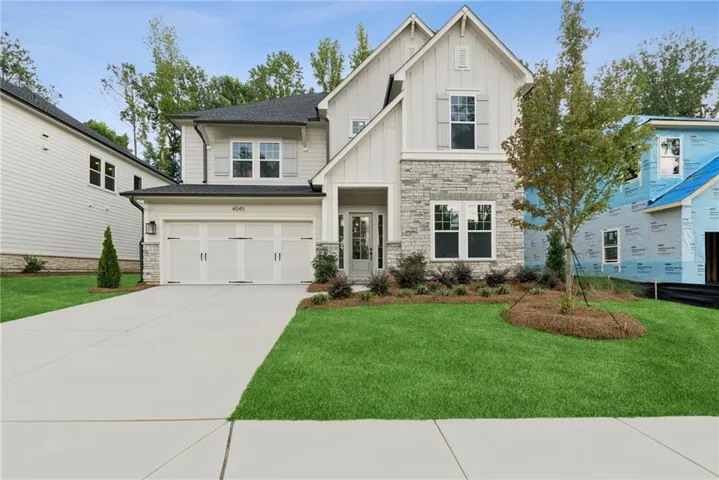 Modern farmhouse style exterior featuring a stone and board-and-batten facade, a two-car garage with carriage-style doors, a concrete driveway, and a manicured lawn with mature landscaping