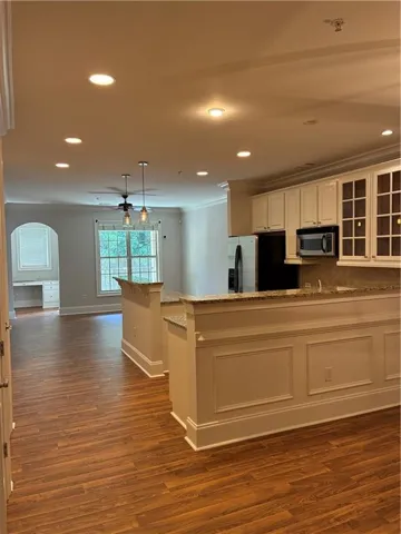 Open-concept interior featuring wood-finish flooring, recessed lighting, a ceiling fan with light fixture, and a kitchen with white cabinetry and a built-in microwave