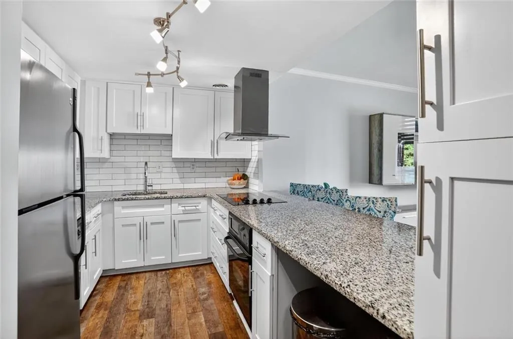 Kitchen with white cabinets, black appliances, dark wood-style flooring, light stone counters, and backsplash