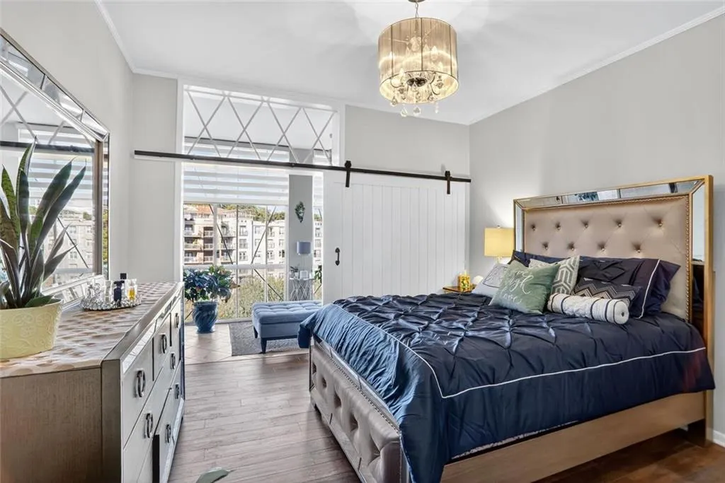 Bedroom featuring hardwood / wood-style flooring, crown molding, a barn door, access to exterior, and a chandelier