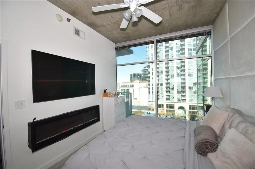 Bedroom featuring a ceiling fan, expansive windows, and a glass covered fireplace