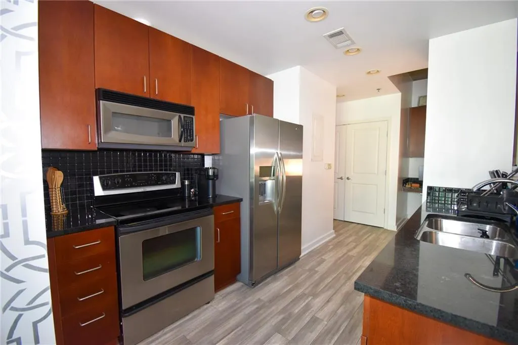 Kitchen with stainless steel appliances, dark stone counters, light wood-type flooring, recessed lighting, and wood finish cabinetry