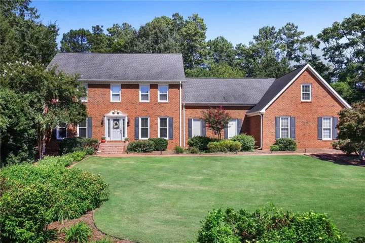 Brick exterior with dark shutters, established landscaping, and a manicured lawn