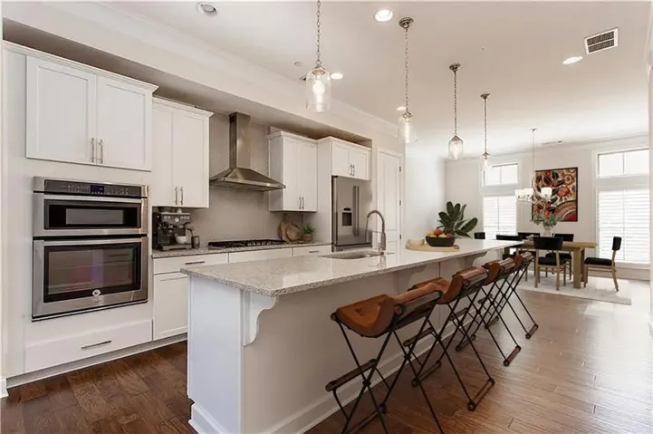 Expansive kitchen featuring white cabinetry, stainless steel appliances, a large center island with a stone countertop, and wood-finish flooring