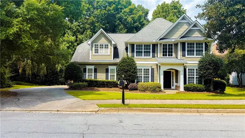 Elegant two-story Colonial featuring a light-colored fiber cement exterior with black shutters, arched entryway, and multi-pane windows