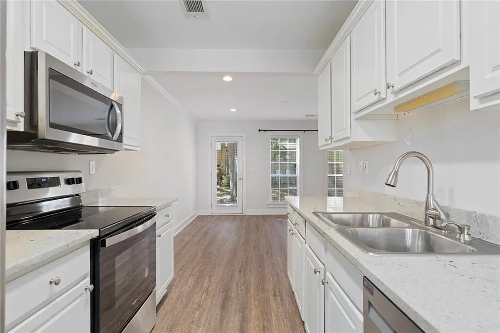 Kitchen featuring stainless steel appliances, white cabinetry, a sink, and visible vents