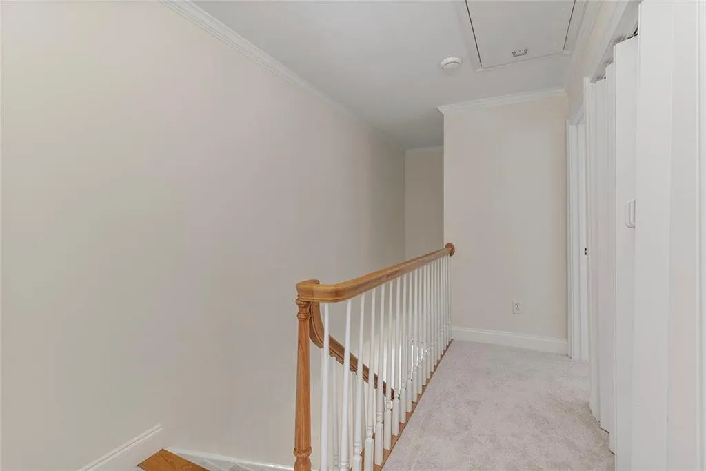 Corridor with attic access, baseboards, light colored carpet, ornamental molding, and an upstairs landing