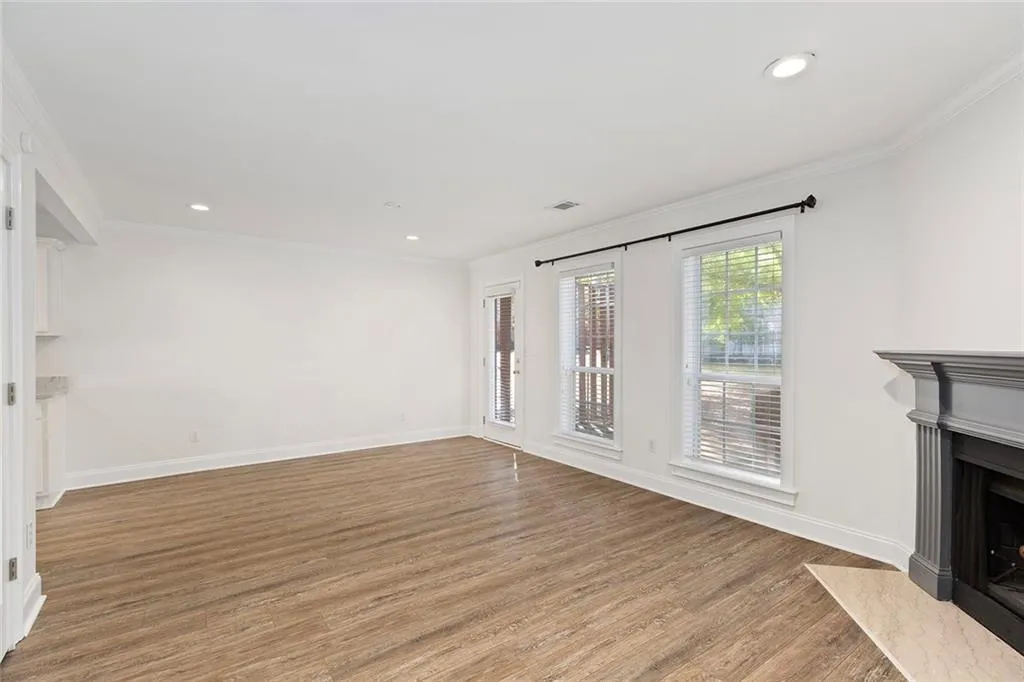 Living room featuring wood finished floors, ornamental molding, a fireplace with flush hearth, and baseboards