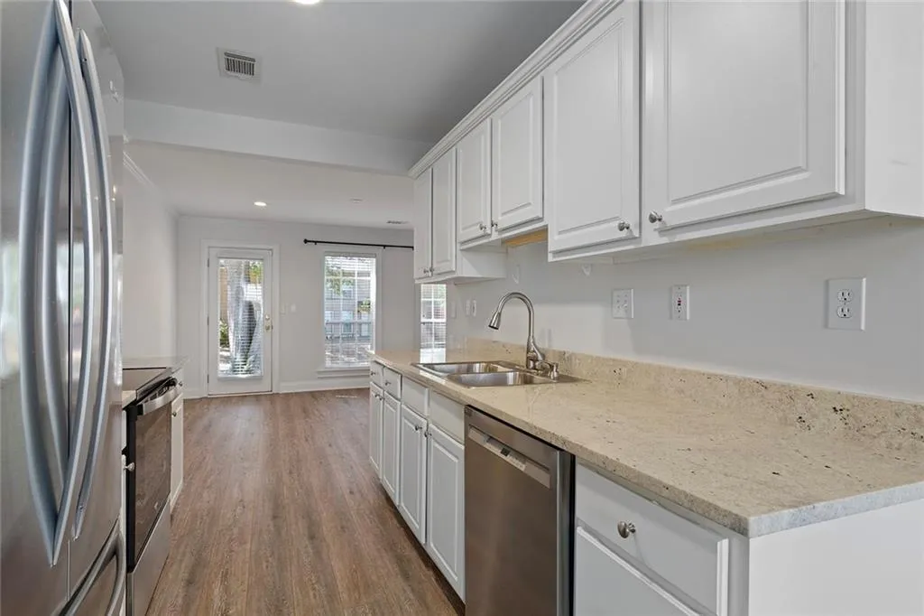 Kitchen featuring light stone counters, a sink, white cabinetry, appliances with stainless steel finishes, and dark wood-style floors