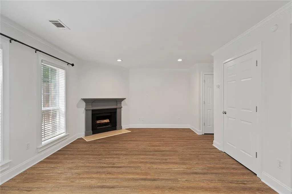 Living room with a fireplace with raised hearth, wood finished floors, visible vents, baseboards, and crown molding
