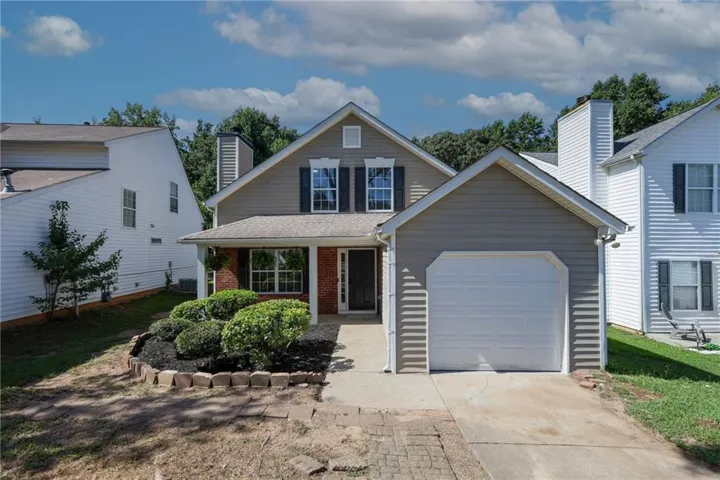 Two-story residence featuring a covered front porch, an attached single-car garage, brick accents, and a landscaped front yard with decorative curbing
