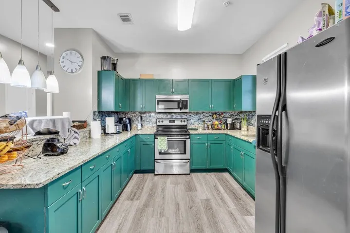 Kitchen with stainless steel appliances, light stone countertops, decorative backsplash, decorative light fixtures, and light wood-type flooring