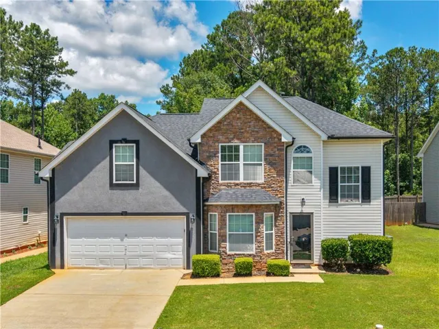 Stately facade featuring a two-car garage, stone accents, dark shutters, a front entry door, and a manicured lawn