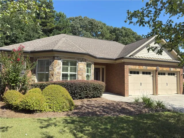 Stone and brick exterior with a two-car garage, multiple windows featuring plantation shutters, and mature landscaping