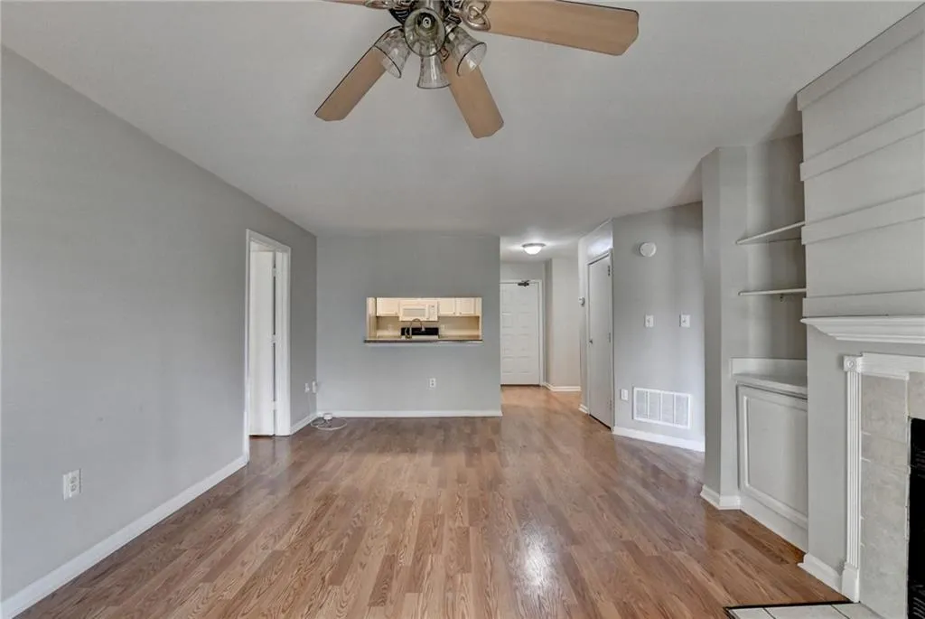 Unfurnished living room featuring a tiled fireplace, ceiling fan, and light wood finished floors