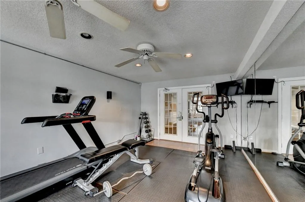 Exercise room featuring french doors, a textured ceiling, recessed lighting, and dark rubber floors