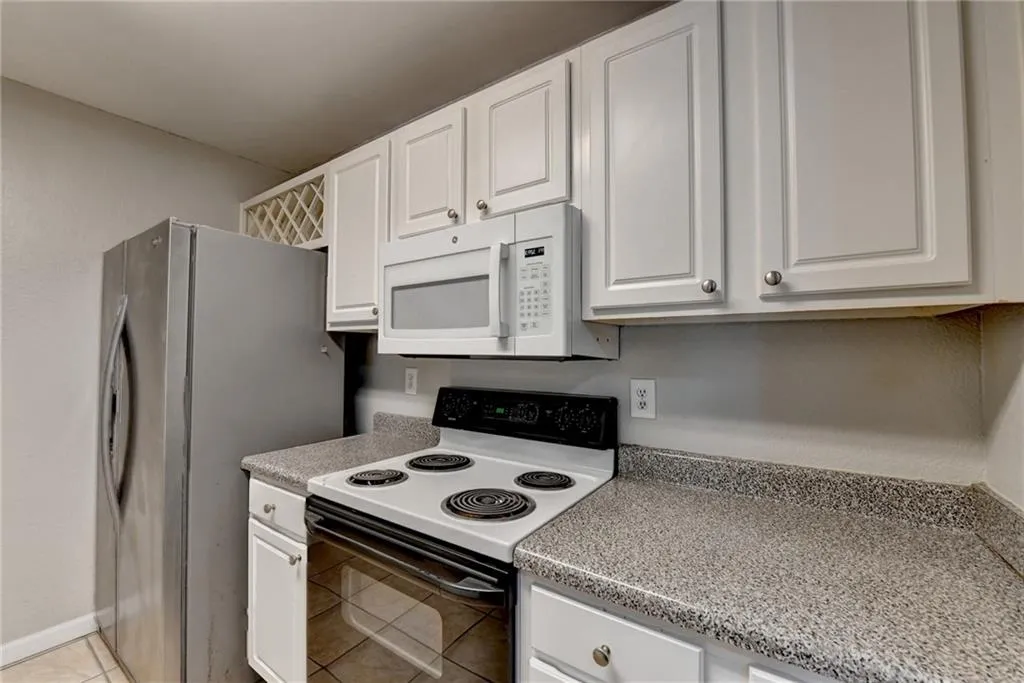 Kitchen featuring electric stove, white cabinets, white microwave, and light countertops