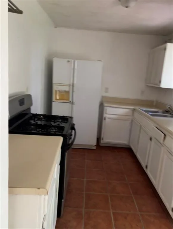 Kitchen with range with gas cooktop, light countertops, white cabinets, dark tile patterned flooring, and white refrigerator with ice dispenser Kitchen with range with gas cooktop, light countertops, white cabinets, dark tile patterned flooring, and white refrigerator with ice dispenser