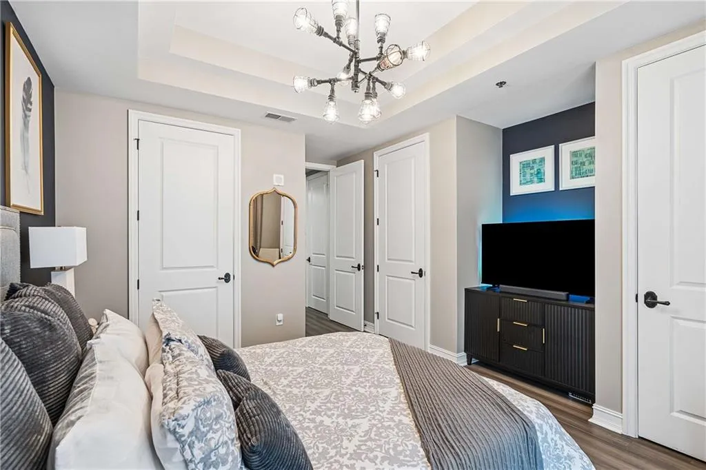 Tray ceiling with a contemporary chandelier, wood-finish flooring, recessed lighting, and panel doors with matte black hardware