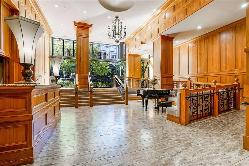 Spacious foyer with wood-paneled walls, a grand staircase, stone-tiled flooring, large windows, and an ornate chandelier