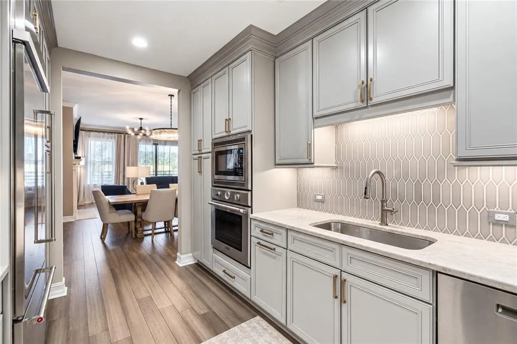 Kitchen featuring gray cabinetry, stainless steel appliances, a tile backsplash, light-colored countertops, and wood-finish flooring