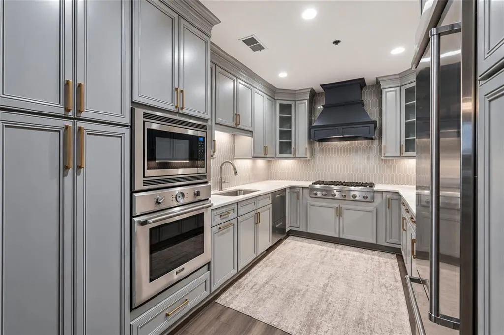 Full-height cabinetry, stainless steel appliances, under-cabinet lighting, light-toned countertops, and a full-height tiled backsplash
