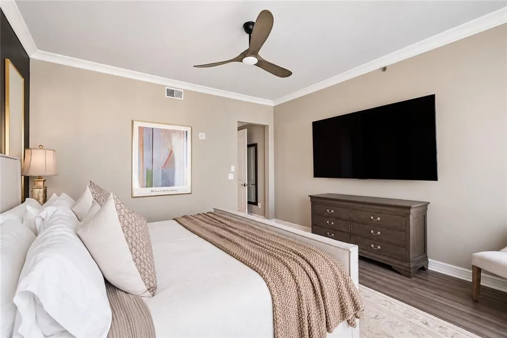 Crown molding, ceiling fan, wood-finish flooring, mounted television, and built-in dresser