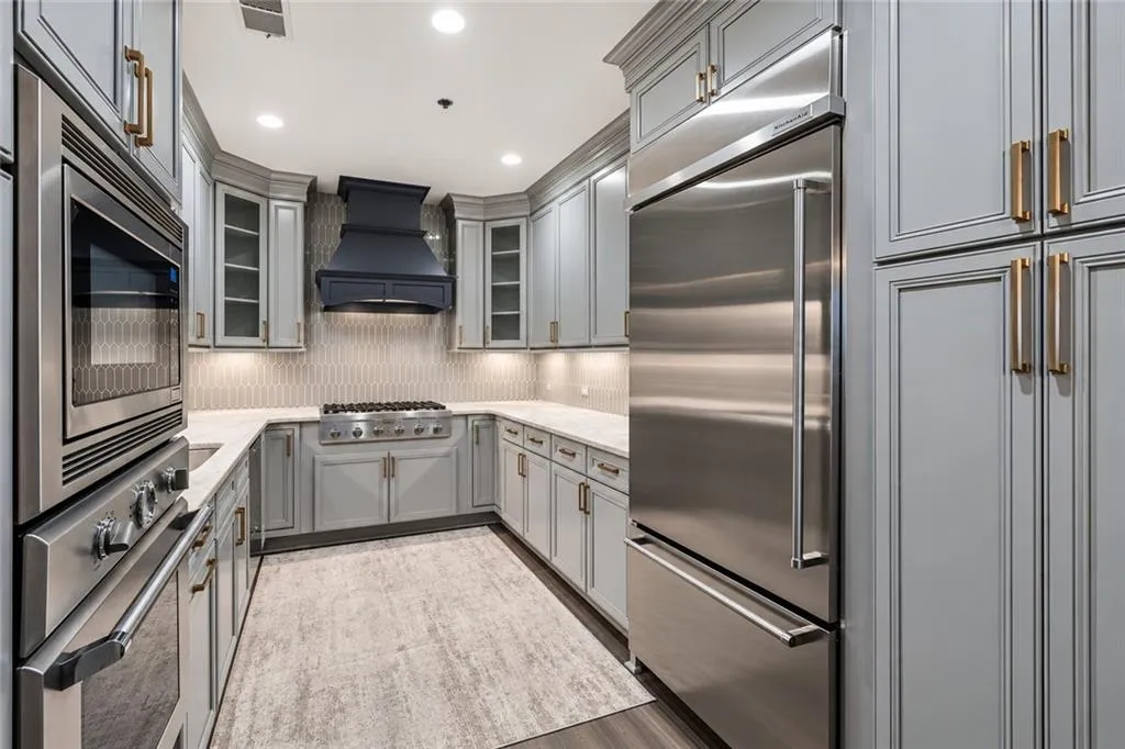 U-shaped kitchen featuring light gray cabinetry, stainless steel appliances, recessed lighting, and a dark blue range hood