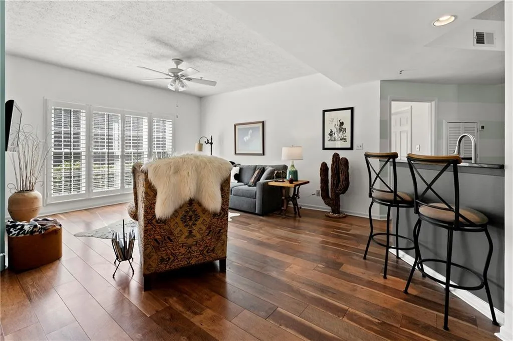Living area with ceiling fan, bright windows and hardwood flooring