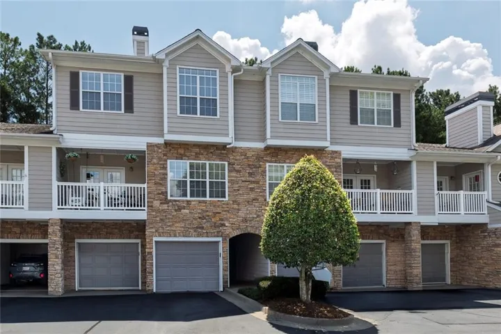 Multi-level facade featuring stone and siding finishes, multiple balconies with white railings, integrated garage doors, and dormer windows