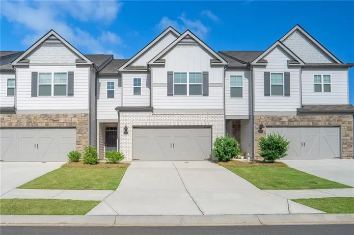 Modern townhome exterior featuring light siding, stone and brick accents, decorative shutters, a single-car garage, and a concrete driveway