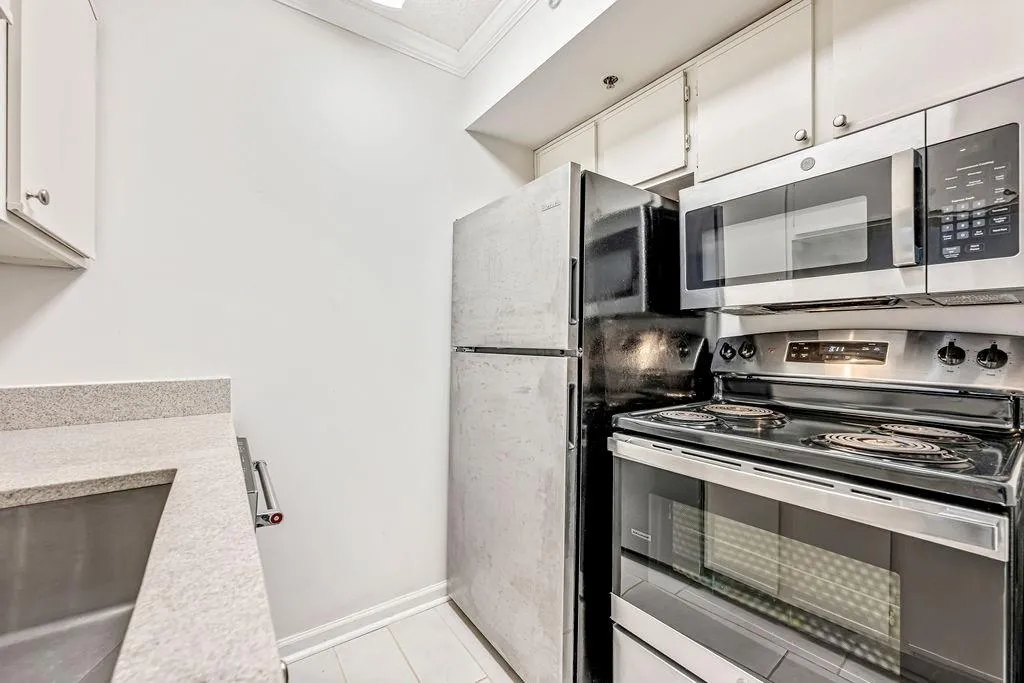 Kitchen with appliances with stainless steel finishes, crown molding, white cabinets, and light stone countertops