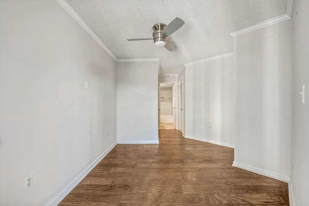 Empty room featuring dark wood-type flooring, a textured ceiling, crown molding, and a ceiling fan