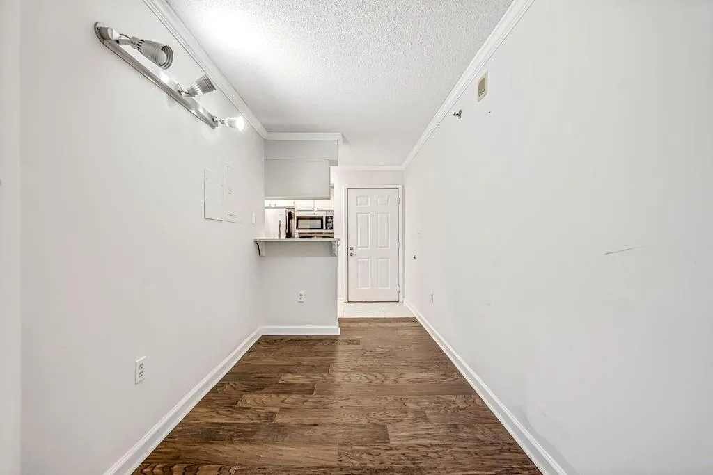 Hallway with a textured ceiling, dark wood finished floors, and ornamental molding