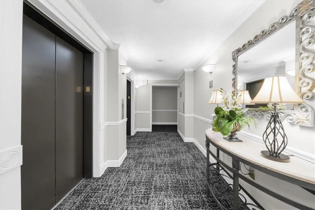 Hallway with elevator, ornamental molding, and dark colored carpet