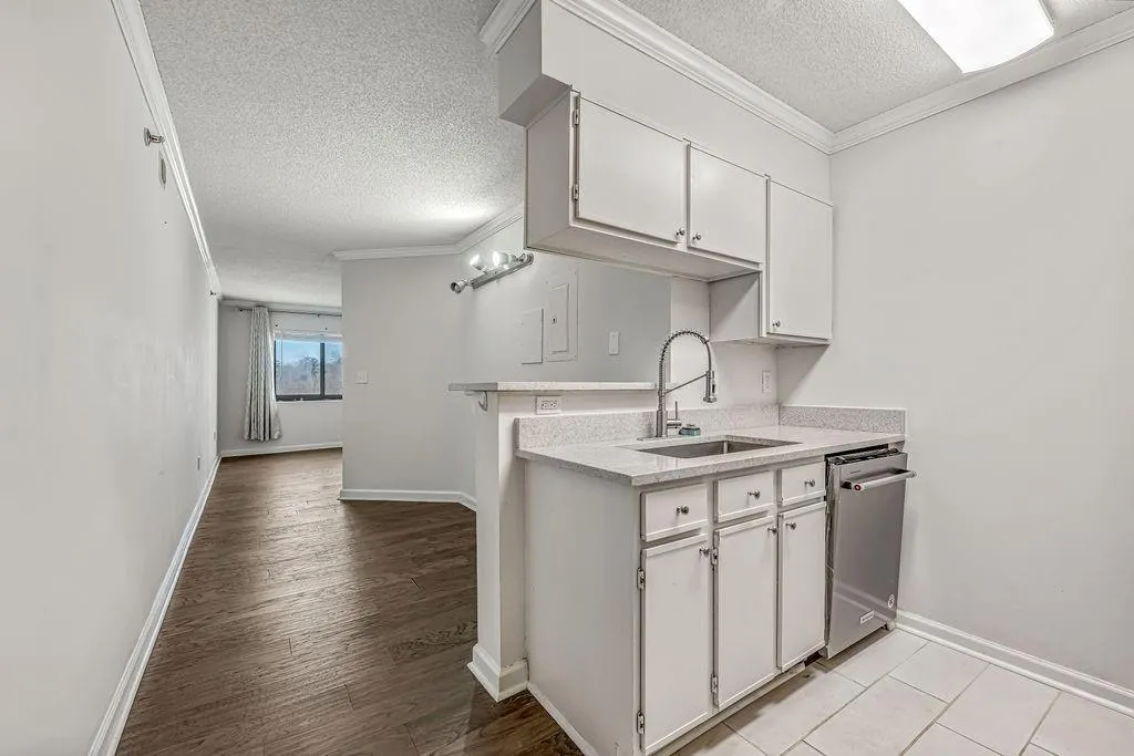 Kitchen with white cabinets, a textured ceiling, crown molding, stainless steel dishwasher, and light stone counters