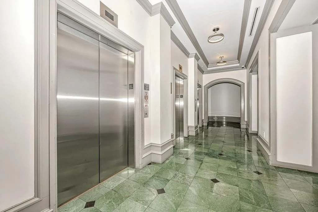 Hallway featuring crown molding, a tray ceiling, elevator, and arched walkways