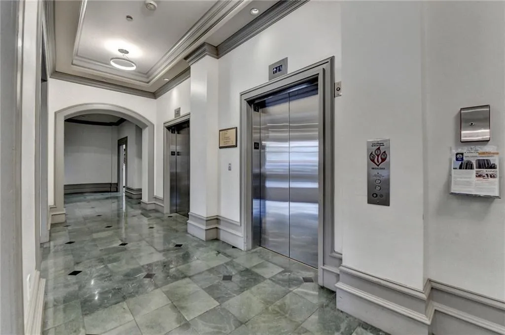 Corridor with crown molding, elevator, arched walkways, and a tray ceiling
