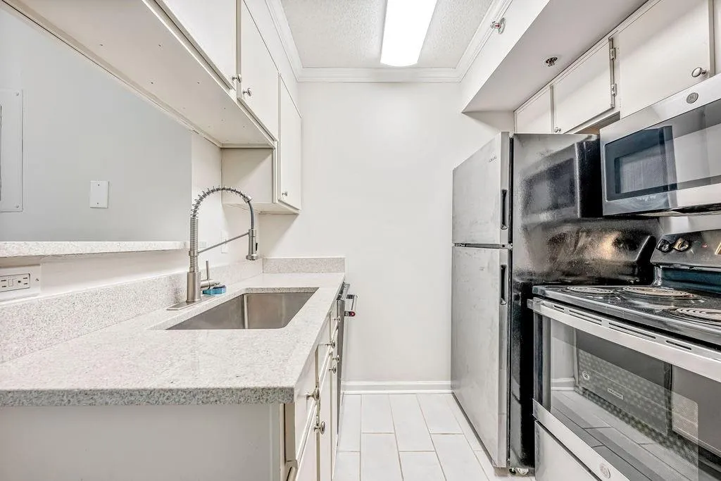 Kitchen with appliances with stainless steel finishes, white cabinetry, crown molding, a textured ceiling, and light stone countertops
