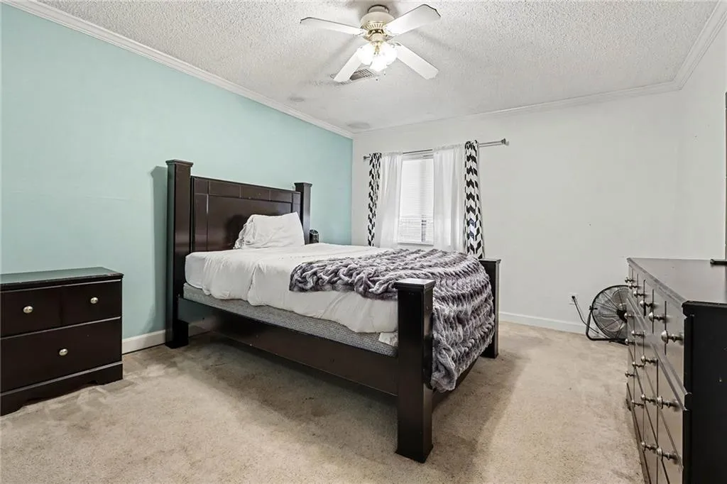 Bedroom with light carpet, a textured ceiling, a ceiling fan, and crown molding