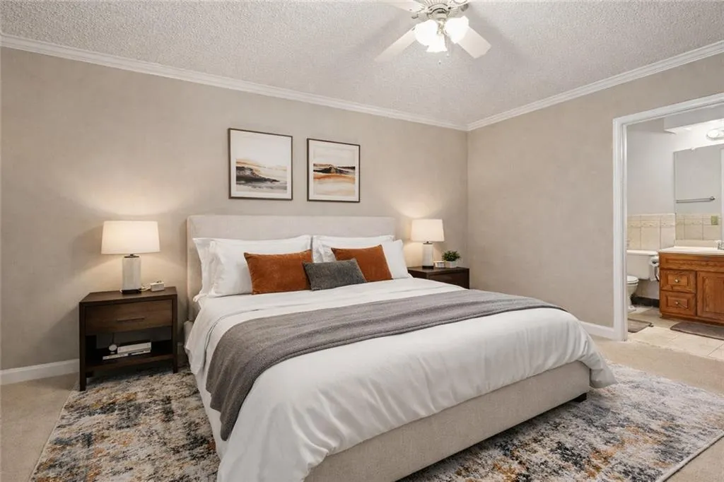 Bedroom with a textured ceiling, crown molding, a ceiling fan, light carpet, and connected bathroom