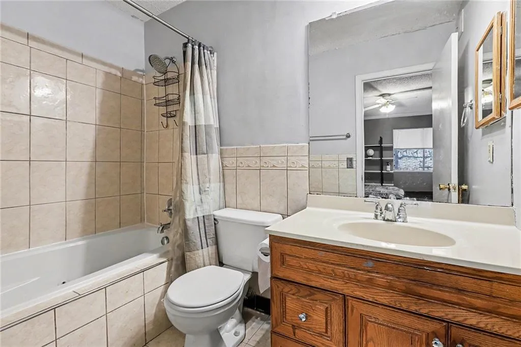 Ensuite bathroom with tiled shower / bath, vanity, a textured ceiling, tile walls, and ceiling fan