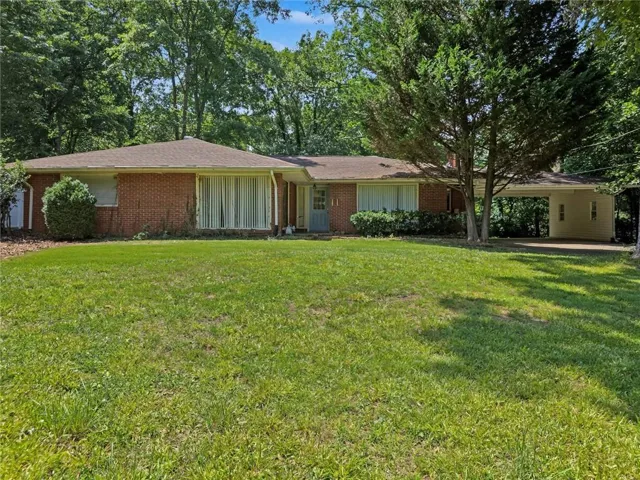 Brick ranch-style home featuring a covered carport, mature front yard landscaping, and a broad picture window