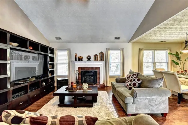 Vaulted ceiling living area featuring wood-finish flooring, a built-in media center, and a brick fireplace with a white mantel