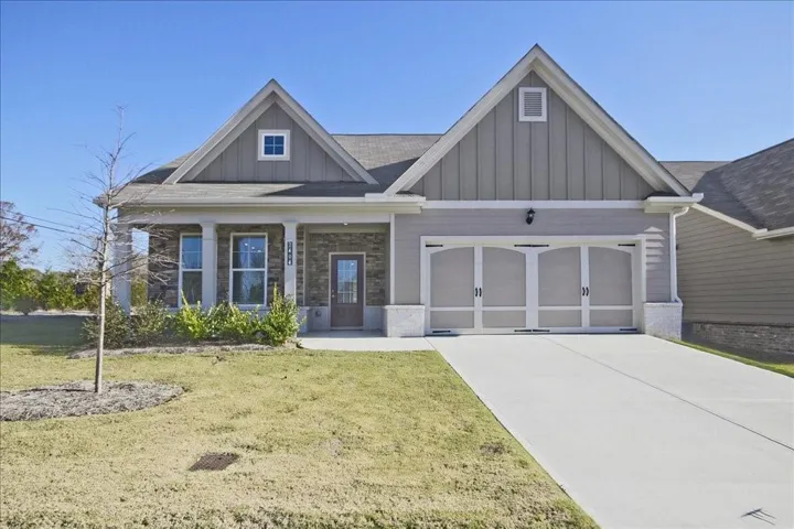 Gabled roofline, stone veneer facade, covered front porch, two-car garage with arched paneling, and a concrete driveway